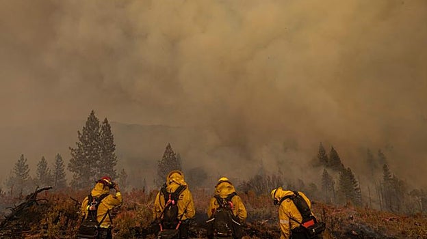 Un grupo de bomberos se resguarda del humo tras una pequeña colina