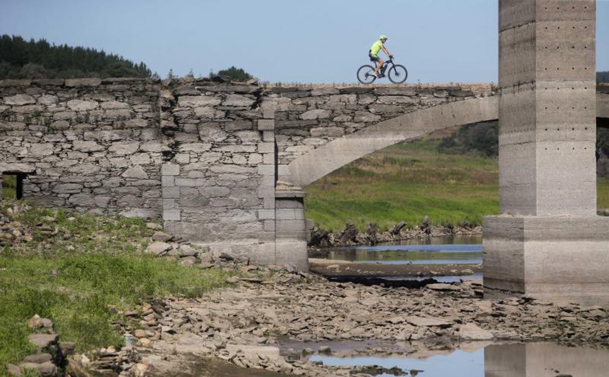 Un ciclista pasa por encima del viejo puente sobre el Miño, sepultado por las aguas en 1962 y visible cuando el cauce transcurre muy bajo