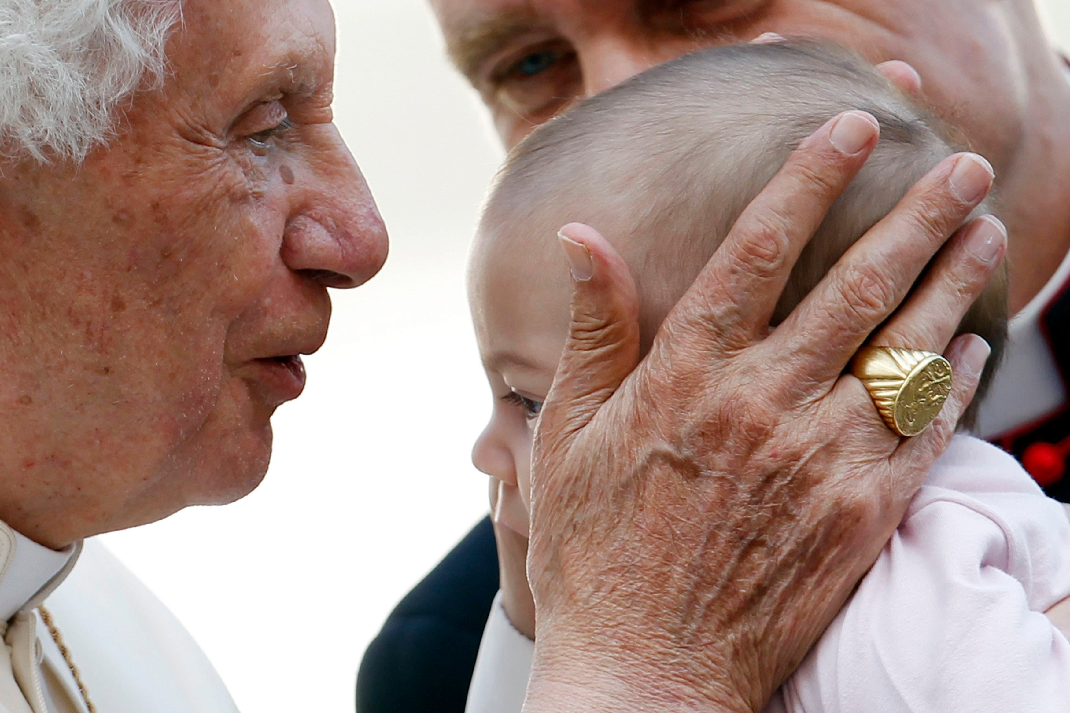 El Papa Benedicto XVI besa a un bebé mientras su principal secretario privado, Monseñor Georg Gaenswein (atrás), sonríe después de la audiencia general del miércoles en la plaza de San Pedro, en el Vaticano, el 24 de octubre de 2012.
