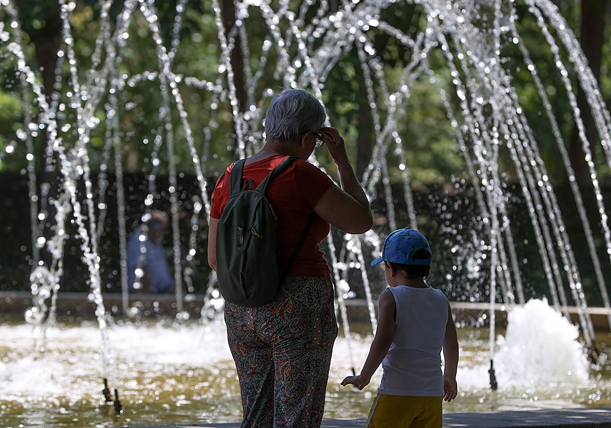 Niños y adultos se refrescan a la sombra, junto a las fuentes públicas del parque del Retiro