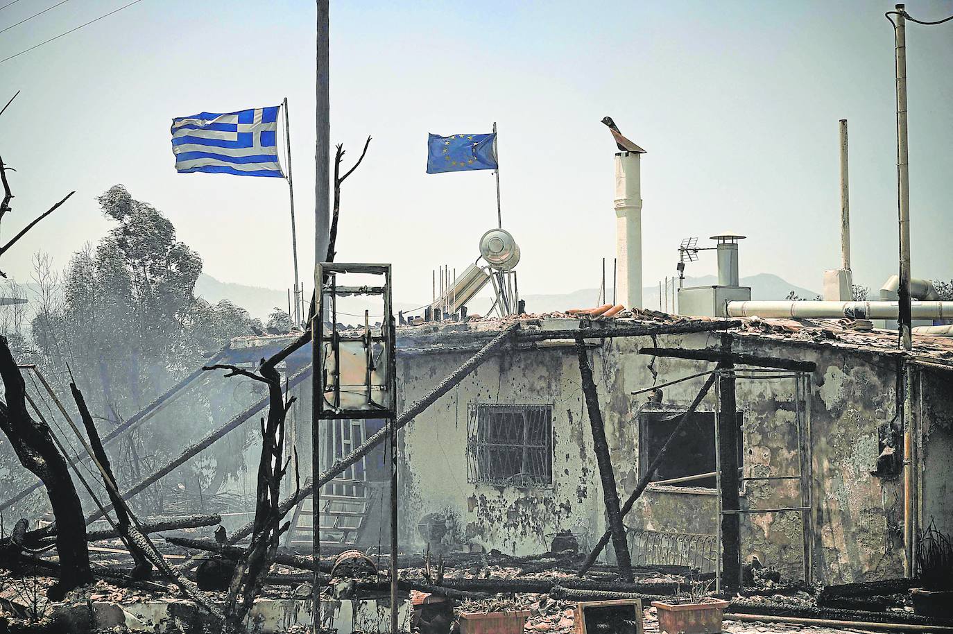 Banderas griegas y europeas ondeando sobre un edificio quemado en medio de un incendio entre los pueblos de Kiotari y Genadi, en la isla griega de Rodas