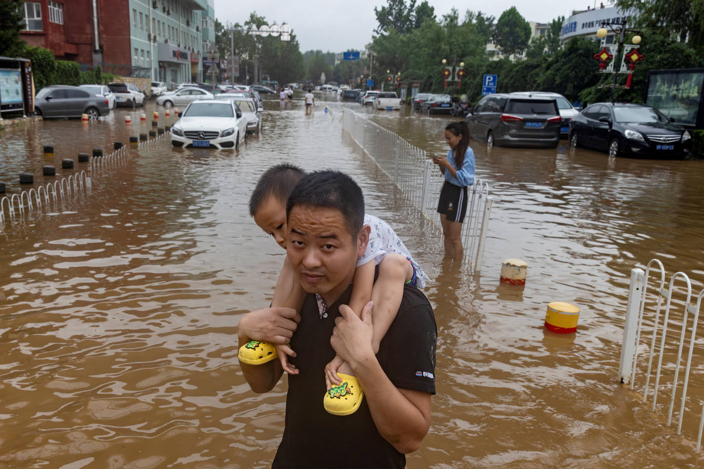 Un hombre con un niño a hombros en una calle inundada en Pekín debido al tifón Doksuri