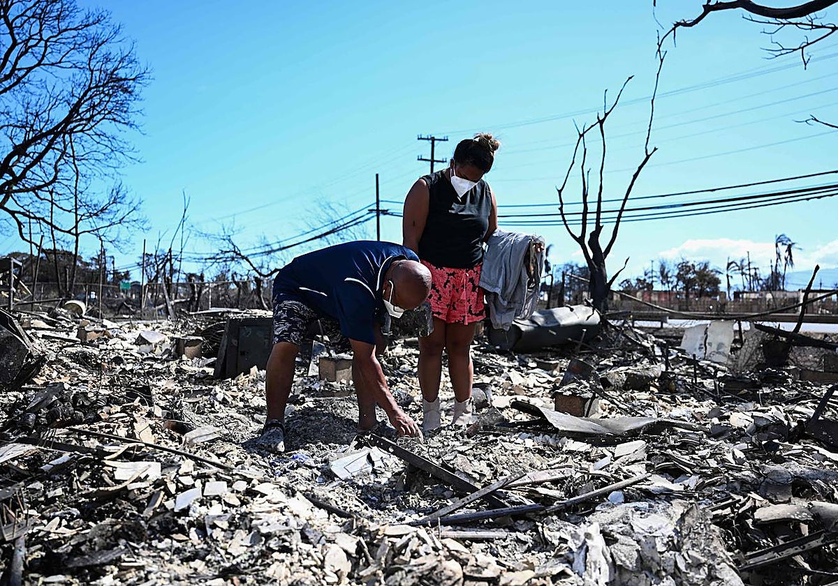 Dos personas buscan sus pertenencias entre las cenizas de su casa quemada por el fuego en Lahaina