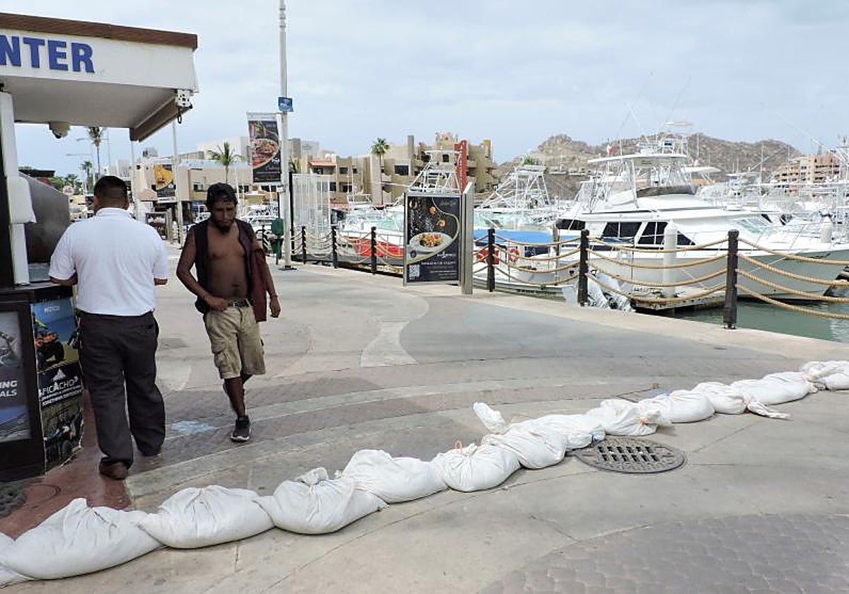 Un hombre camina junto a sacos llenos de arena mientras sale de la marina mientras el huracán Hilary de categoría 4 se precipita hacia la península de Baja California en México, en Cabo San Lucas, México.