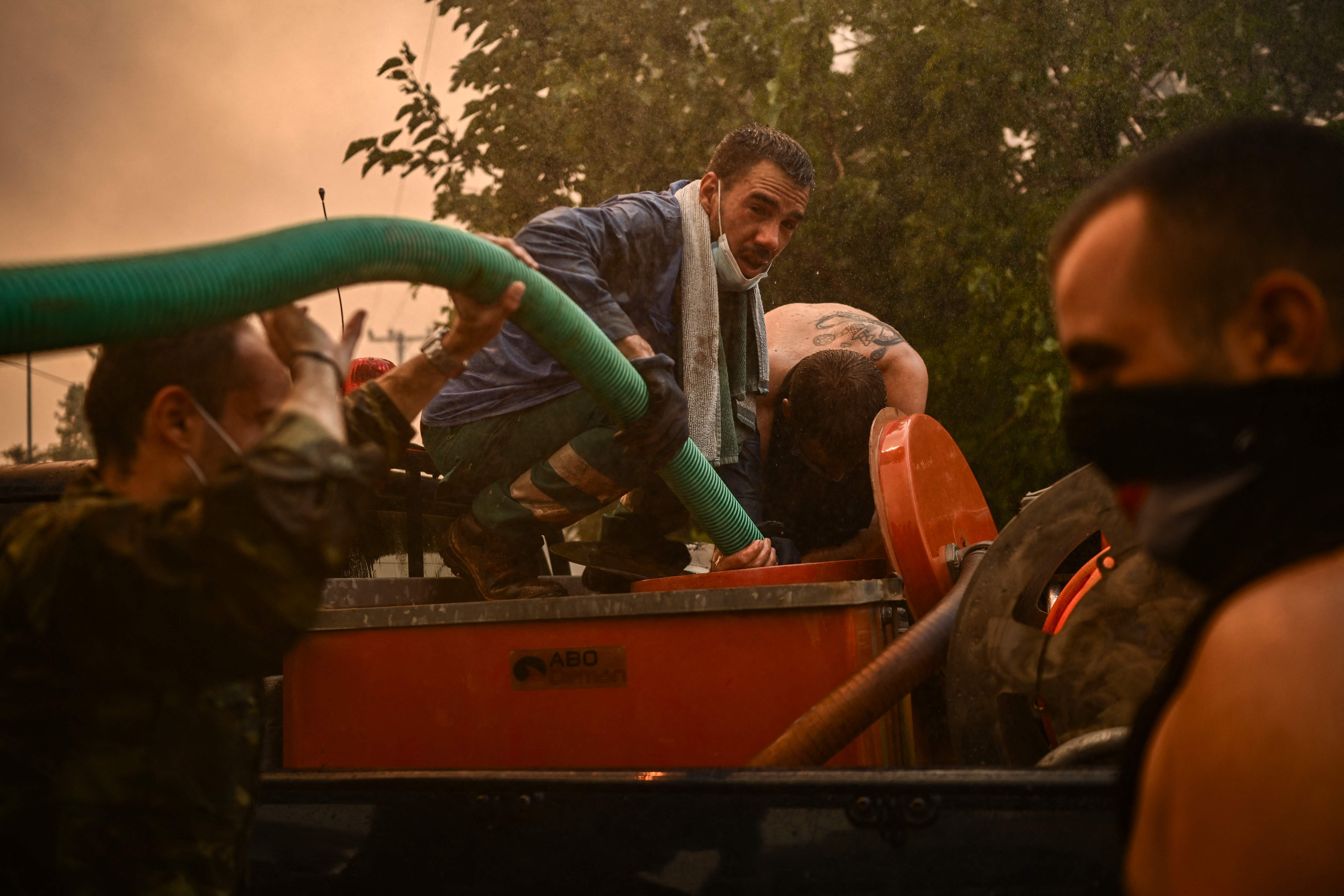 Varias personas reciben agua de un camión durante el incendio en Chasia, a las afueras de Atenas 