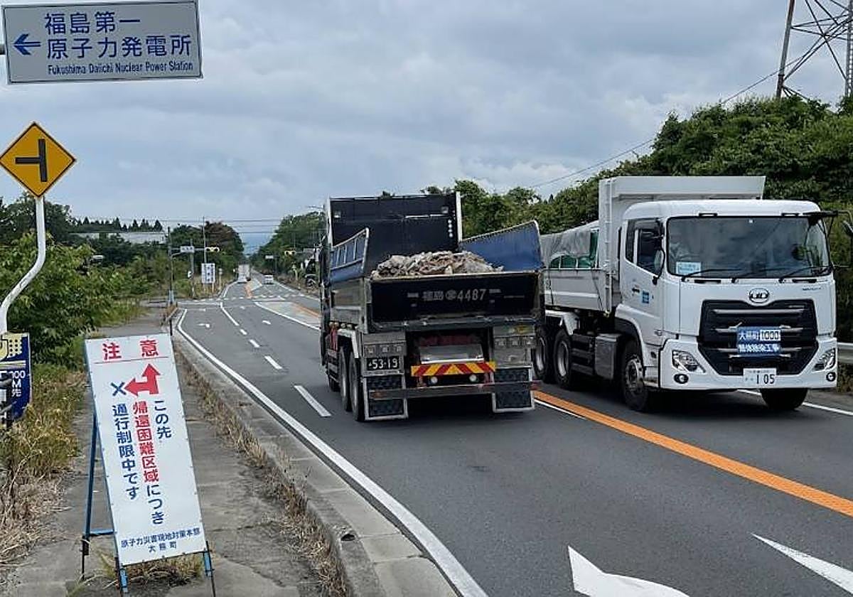 Dos camiones que participan en el desmantelamiento de la central de Fukushima pasan bajo la señal que indica su carretera de acceso, cortada al tráfico por la alta radiación