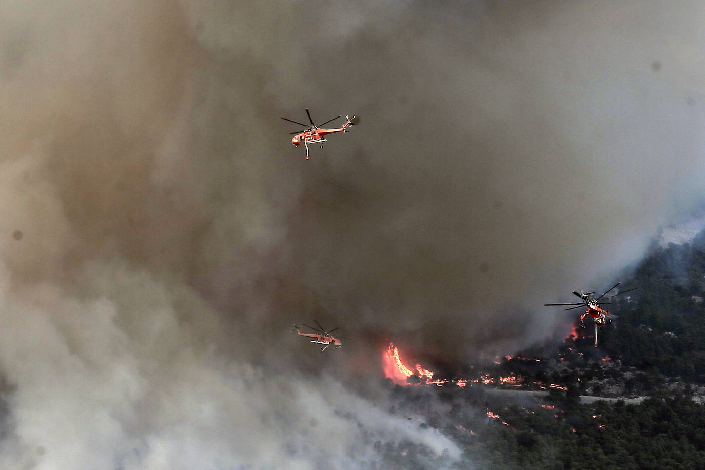 Un grupo de helicópteros de extinción de incendios opera durante un incendio forestal en la montaña Parnitha, en las afueras de Atenas