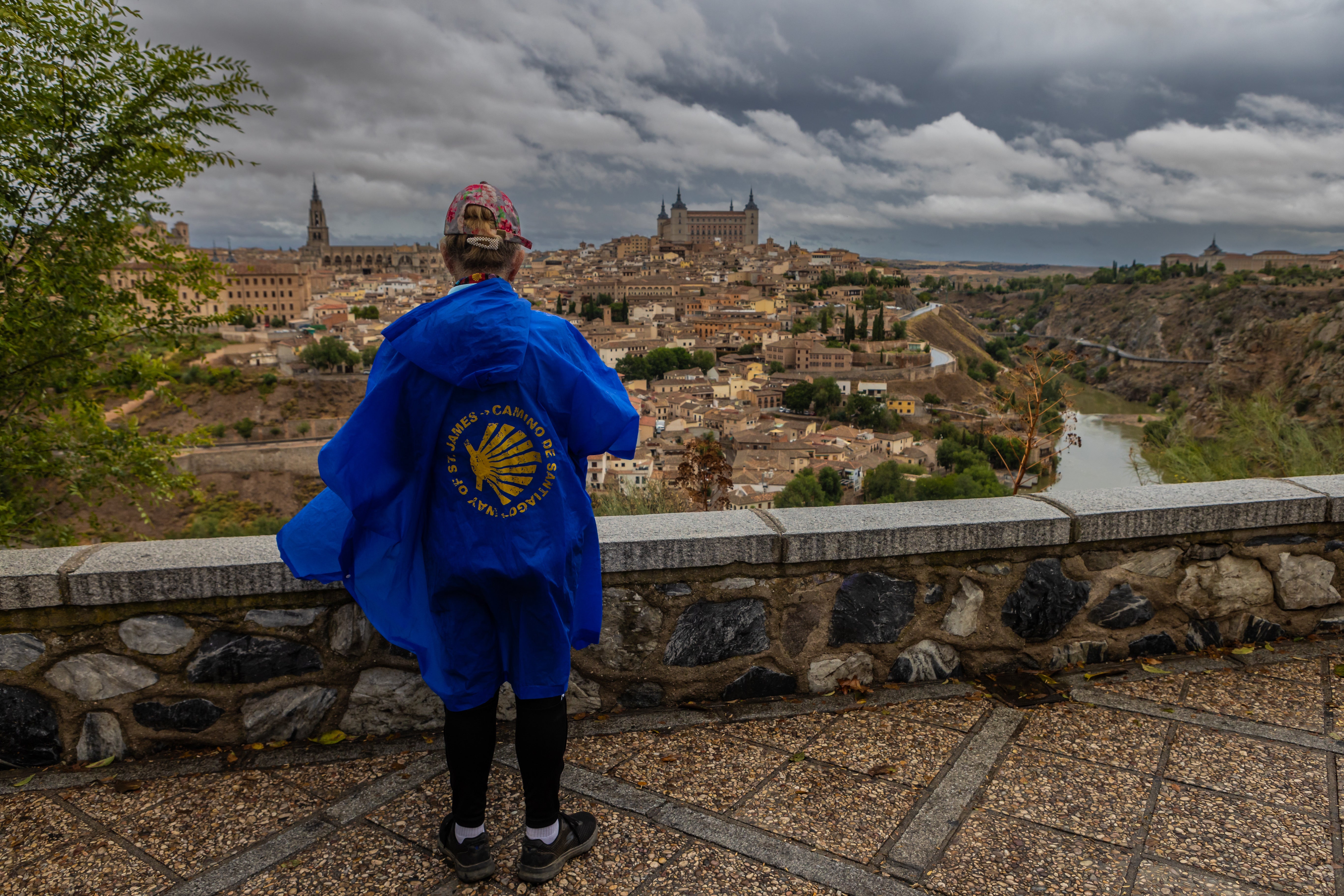 Una persona fotografía la ciudad de Toledo desde el mirador del Valle, ataviada con un poncho para la lluvia