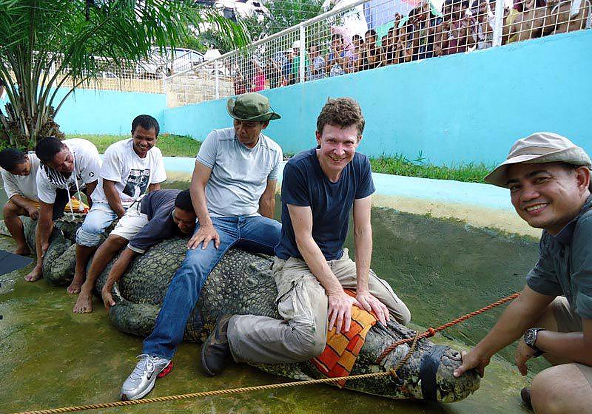 El zoólogo Adam Britton encima de la cabeza de un cocodrilo en el zoo en el que trabajaba