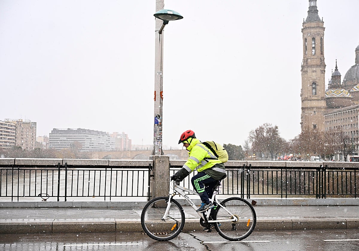 Una persona camina en bicicleta bajo la nieve en Zaragoza