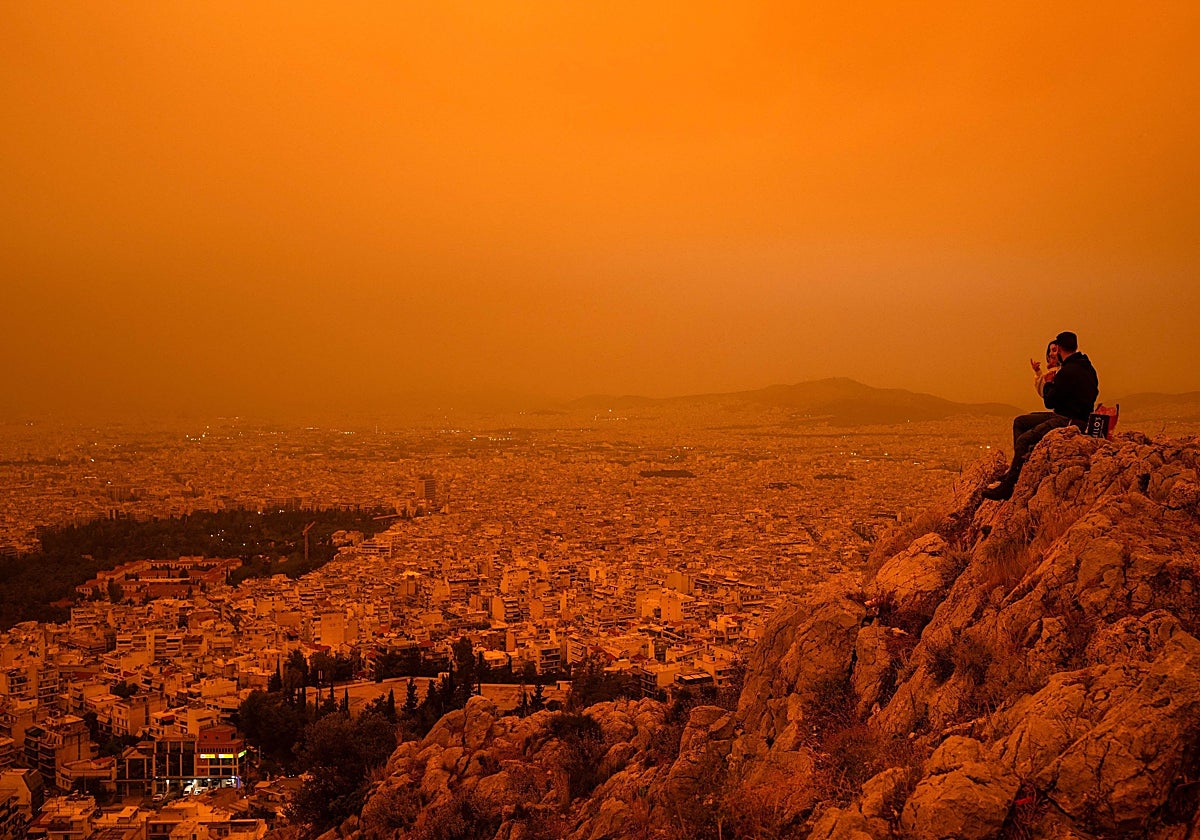 Una pareja sentada en la colina de Tourkovounia, mientras los vientos del sur arrastran oleadas de polvo sahariano, en Atenas