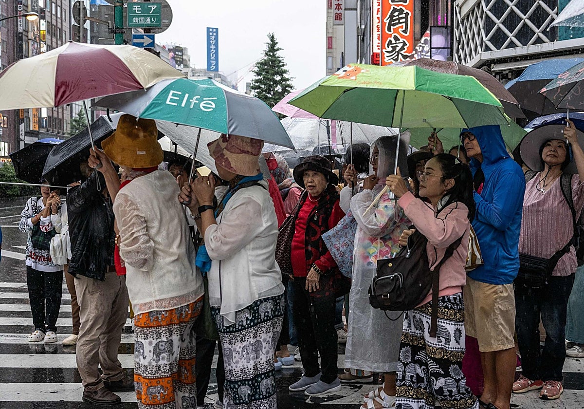 Un grupo de turistas con paraguas para protegerse de la lluvia esperan para cruzar una calle en Shinjuku, Tokio