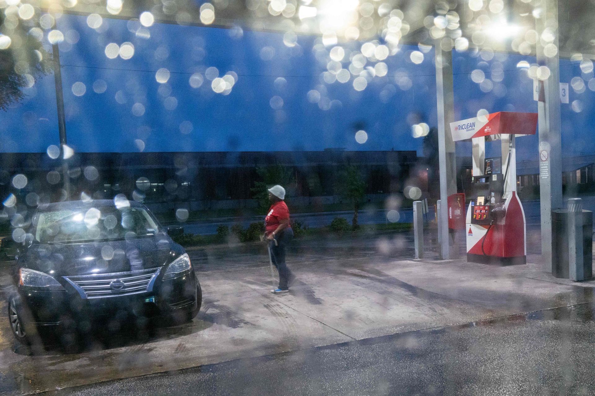 Una ciudadana reposta en una gasolinera con las luces en las oscuridad y la lluvia en la cámara