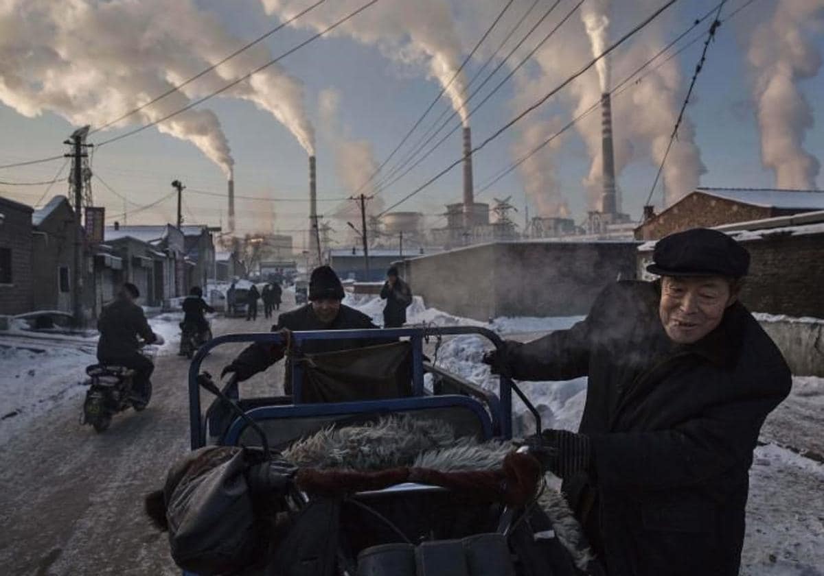 Un hombre chino empuja su triciclo con las chimeneas de una planta a carbón en Shanxi, China