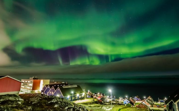 Imagen principal - Las luces verdes sobre el cielo de Nuuk City (Groenlandia) en una noche de septiembre. Debajo, un cazador inuit del norte de Groenlandia se desplaza con su trineo de perros sobre el mar helado. En la última foto, Britta Mortensen es una de las 4.000 mujeres inuit a las que le fue implantado un dispositivo anticonceptivo sin su consentimiento