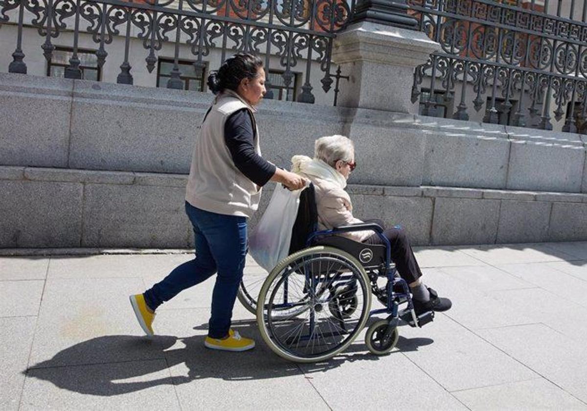 Una mujer mayor en silla de ruedas y su cuidadora pasean por el centro de Madrid en una imagen de archivo