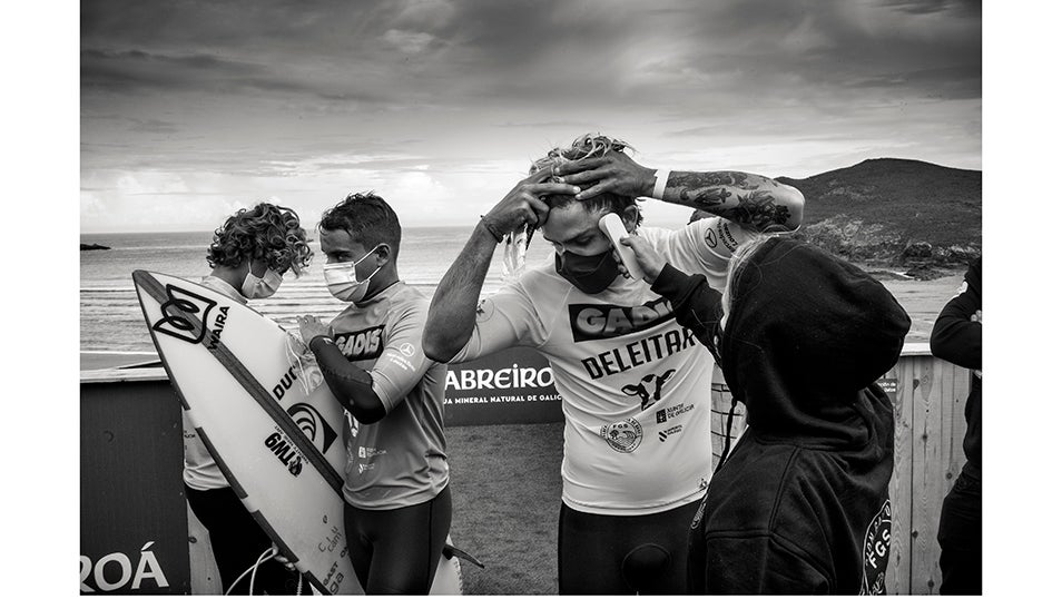 Un grupo de surfistas de élite se toma la temperatura antes de entrar al mar para competir en el campeonato profesional de surf Pantín Classic en Galicia. Este año, el campeonato profesional de surf Pantín Classic, que forma parte del circuito internacional de surf, se celebró después del estado de emergencia decretado por el gobierno español debido a la pandemia de COVID-19. Aunque el estado de alarma ya no estaba activo, el virus seguía siendo una amenaza muy real para los atletas que competían en el evento, los organizadores y el público. Por lo tanto, la organización tomó todas las medidas de seguridad posibles para hacer del campeonato un entorno seguro frente al COVID-19. Se estima que la pandemia ha causado más de 70.000 muertes en España, de las cuales más de 50.000 han sido confirmadas mediante prueba PCR. La gran mayoría de los fallecidos eran personas mayores de 65 años. Según un estudio de seroprevalencia, hasta junio, el 5% de la población española había sido infectada por el virus.
