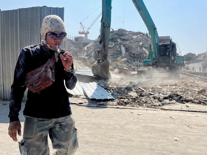Hombre fumando un cigarro cerca de un edificio destruido