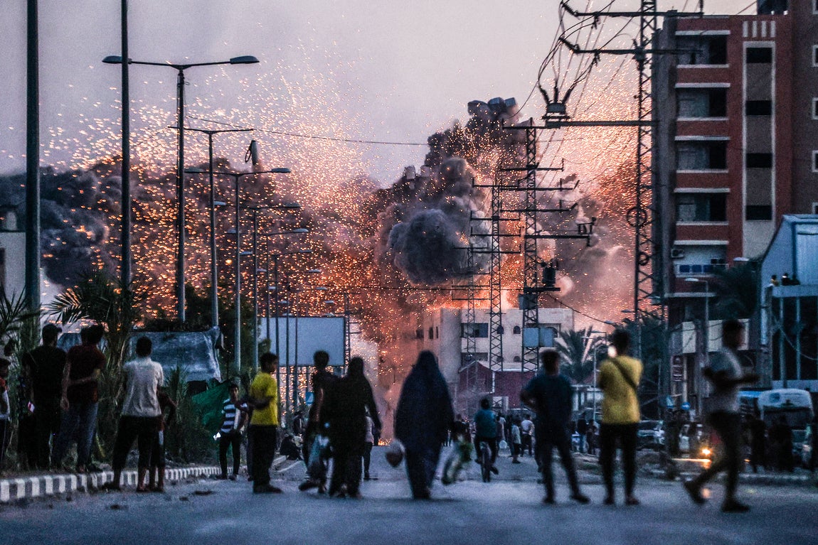 La gente observa cómo el humo y las llamas se elevan sobre un edificio, tras los ataques israelíes en Deir al-Balah. Israel bombardeó la ciudad central de Gaza varias veces a lo largo del año