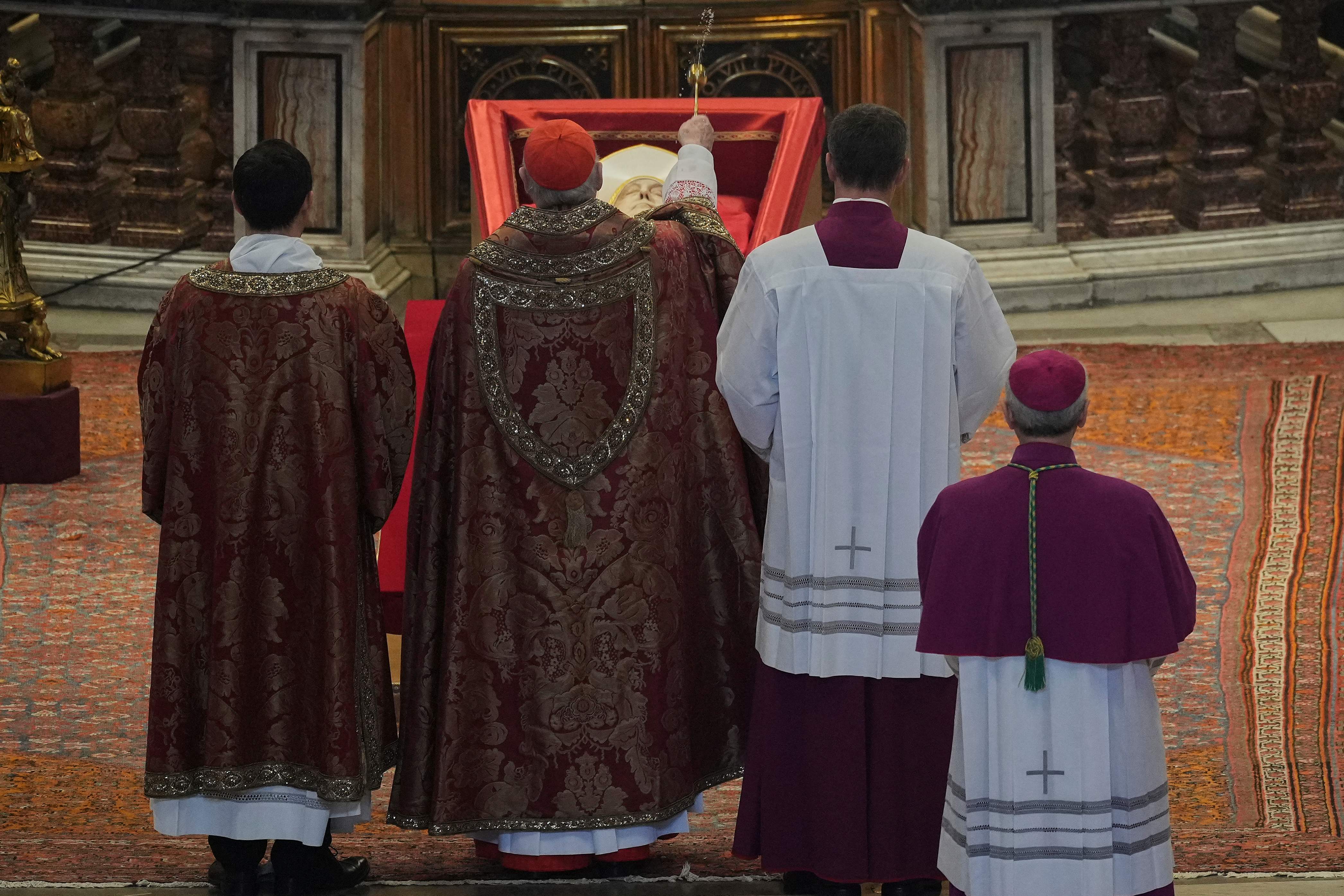 El cardenal camarlengo Kevin Joseph Farrell (centro), flanqueado por el maestro de ceremonias, monseñor Krzysztof Marcjanowicz (izq.), y el arzobispo Diego Giovanni Ravelli, bendice el cuerpo del papa Francisco.