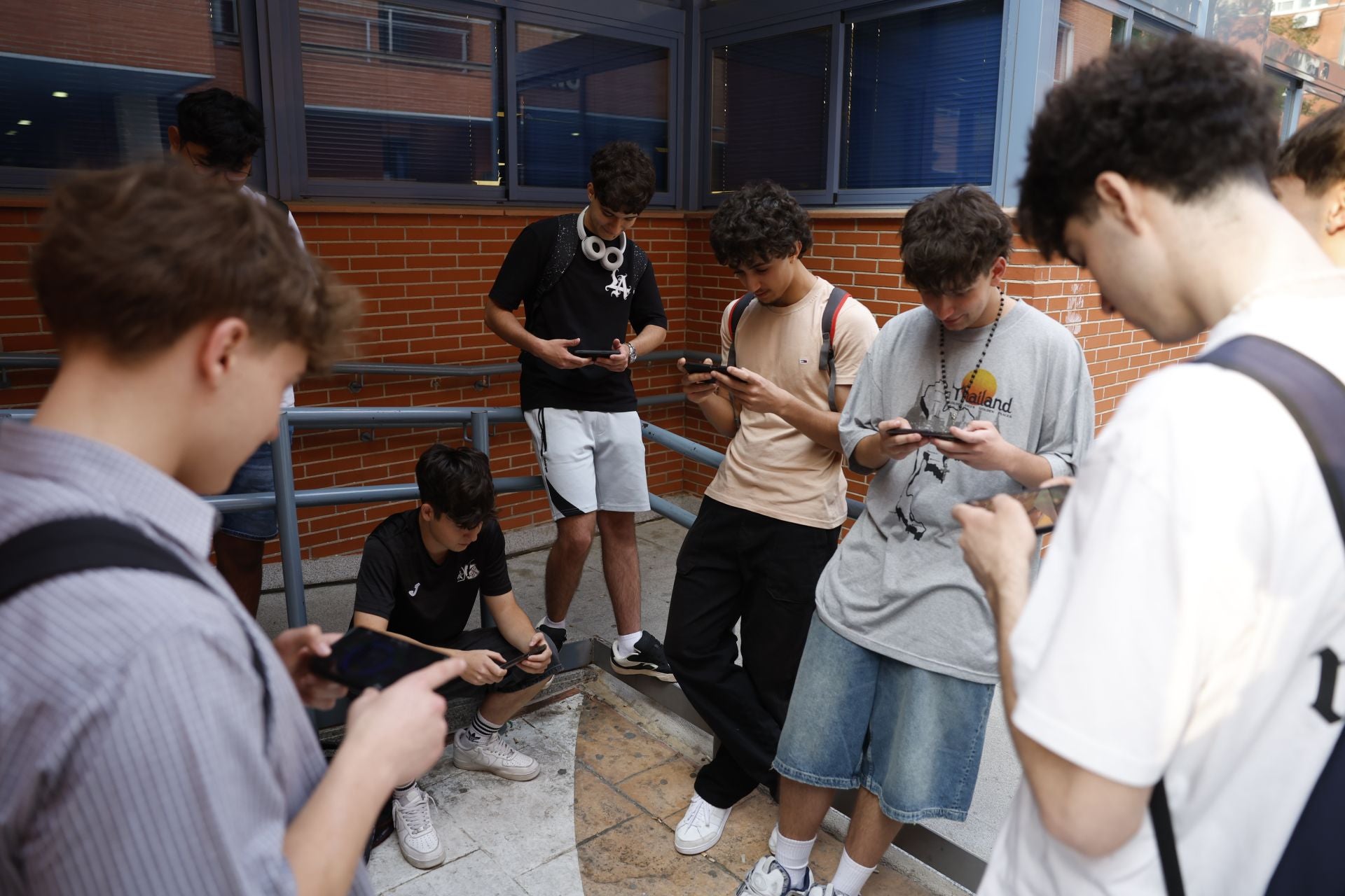 Varios estudiantes ojean sus teléfonos móviles mientras esperan a que se abran las aulas para someterse a la Prueba de Acceso a la Universidad (PAU) en la Universidad Complutense de Madrid.