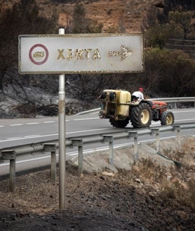 Imagen secundaria 2 - Un vehículo calcinado a la entrada de Xerta. Sobre estas líneas, Susi Gómez, con Lita en sus brazos. A la derecha, un campesino en su tractor, tras levantarse el confinamiento por las llamas. 