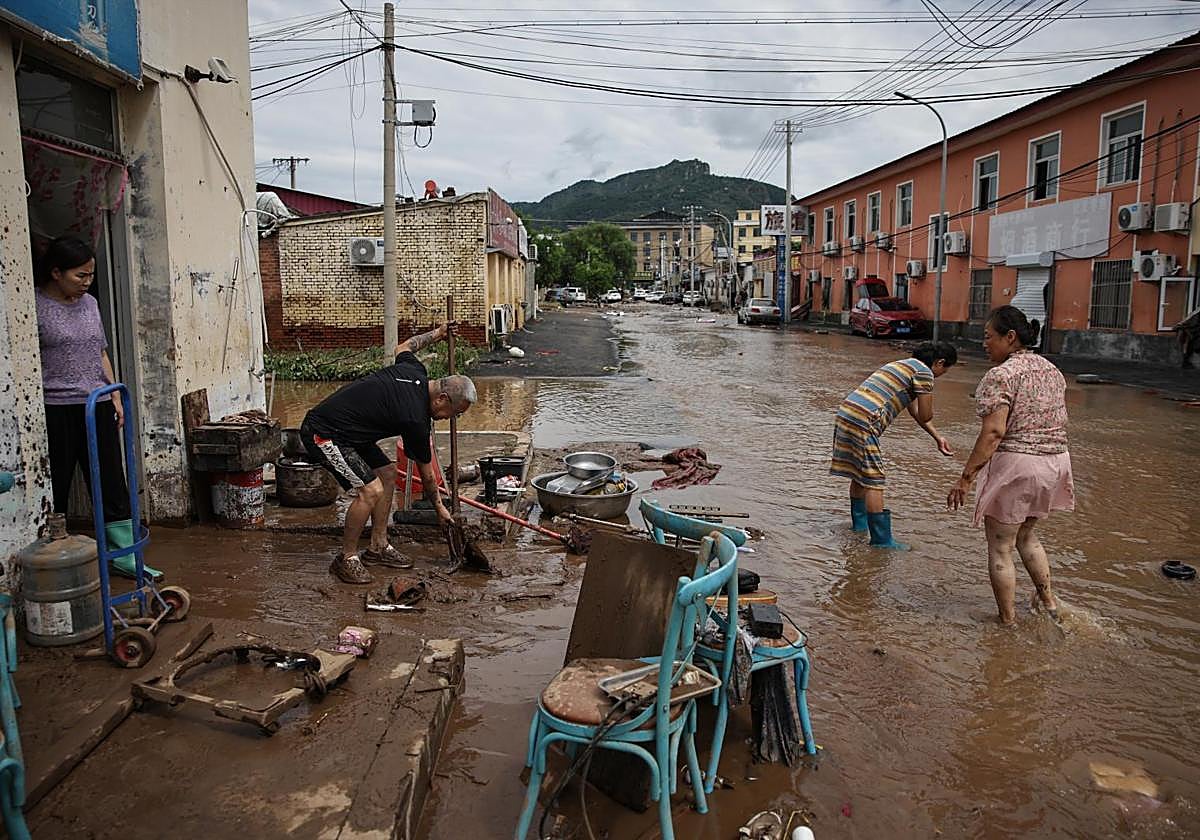 Un grupo de personas limpian el barro en la entrada de un restaurante en una calle inundada en Taishitun, en el distrito de Miyun, Pekín, China