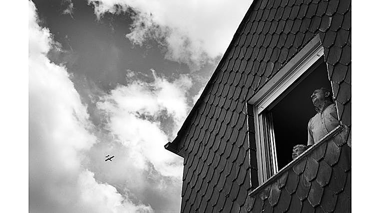 Dos vecinos observan desde la ventana de su casa el paso de un hidroavión. La mirada atenta refleja la preocupación de quienes siguen desde sus hogares la evolución de un incendio que mantiene en vilo a todo el valle. En Fornela, varios pueblos han sido evacuados de manera preventiva y otros permanecen en alerta. La incertidumbre se mezcla con la tensión de no saber si las llamas alcanzarán las viviendas. El paso de los medios aéreos es, para muchos vecinos, la única señal visible de que el esfuerzo por salvar el valle no se detiene.
