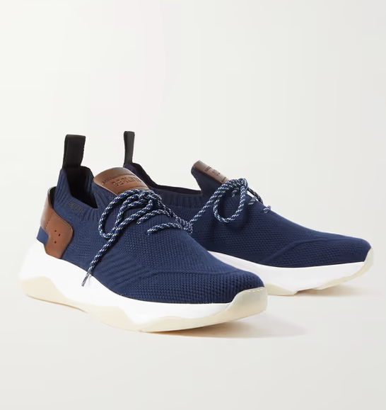 Berluti firma estas zapatillas de lujo en color azul marino confeccionadas tejido ligero elástico y adornadas con el característico cuero Venezia de la firma. Llevan una cómoda suela de goma, tienen una plantilla acolchada y tanto el talón como la puntera van perfectamente reforzados. Precio: 1150 euros.