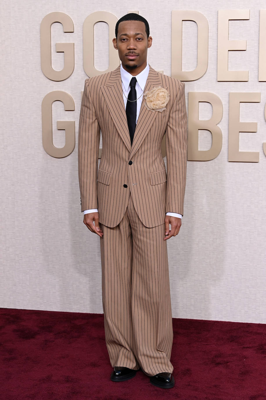 Tyler James Williams con traje beige a rayas y flor XXL en la solapa. 