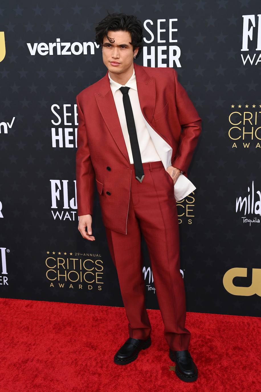 Charles Melton con un traje en color rojo con solapas cruzadas. 