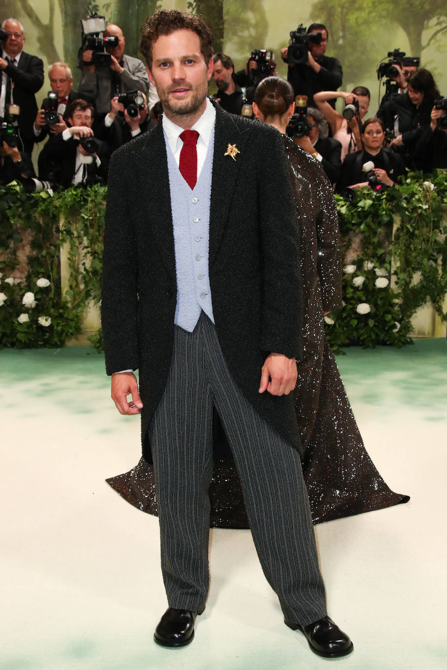 Jamie Dornan se vistió de chaqué de Loewe que incluía levita negra, pantalón gris de rayas, chaleco azulado y corbata roja. En la solapa lució un broche, el accesorio estrella entre los hombres más estilosos. 