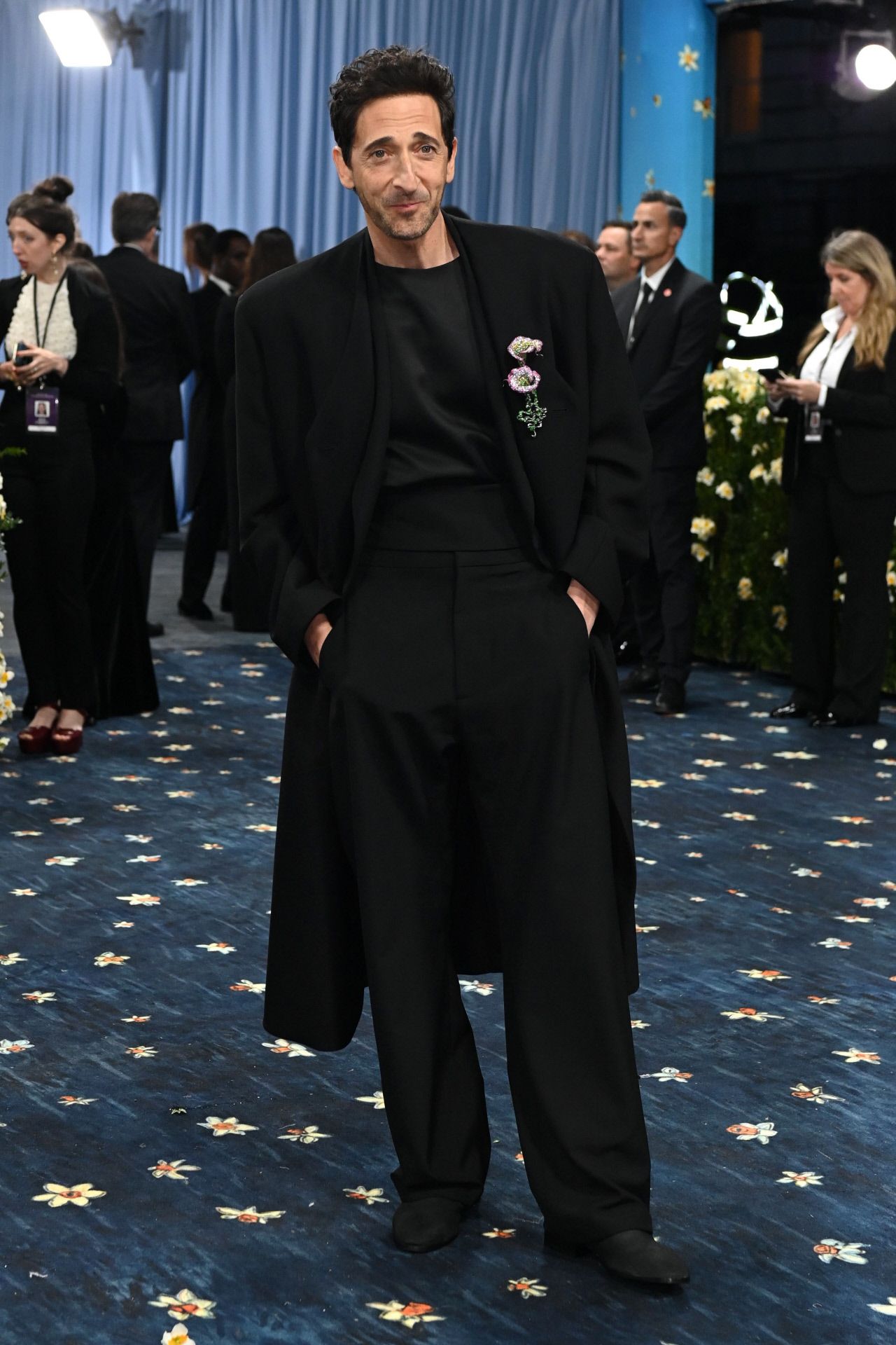 Adrien Brody se decantó por un total look en color negro, formado por un abrigo, camisa y pantalón ancho. El actor añadió un llamativo broche. 