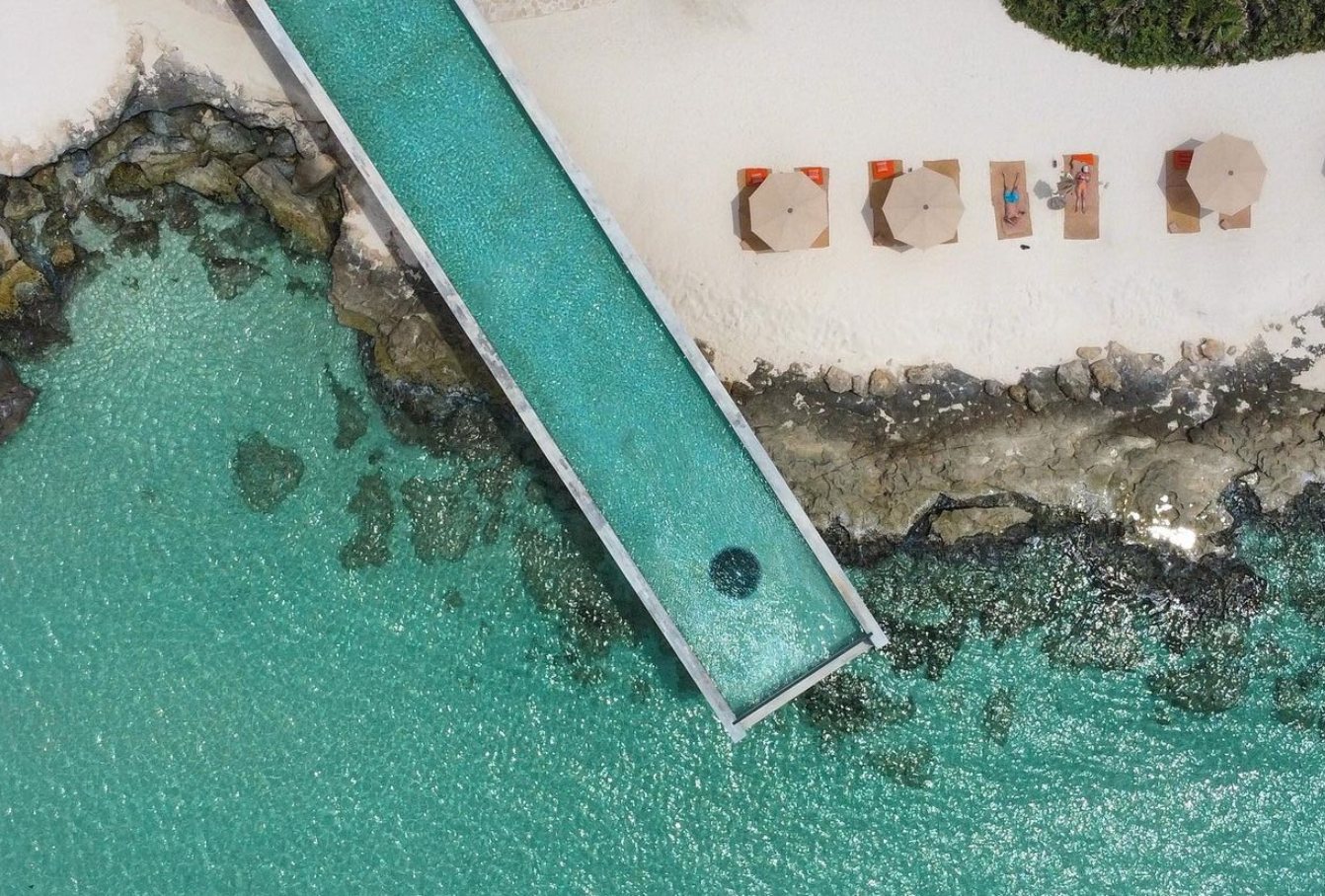 En la Riviera Maya, México, La Casa de la playa invita a los huéspedes a un mundo de tranquilidad junto al mar. La estética de este complejo todo incluido presenta un diseño en piedra que recuerda a los antiguos templos mayas combinado con grandes ventanales de suelo a techo que permiten disfrutar de las vistas en todo momento. Cuenta con 63 suites decoradas con obras de arte y artesanía local que incluyen una terraza con tumbonas y bañera de hidromasaje tallada en roca volcánica, cuatro restaurantes que ofrecen lo mejor de la gastronomía mexicana y latinoamericana, un spa holístico y una increíble piscina infinita elevada con vistas al mar Caribe que se ha convertido por derecho propio en la imagen estrella del hotel en las redes sociales.