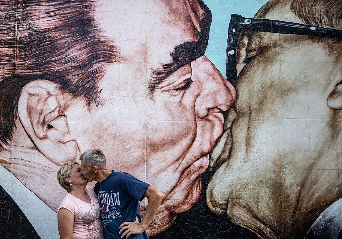 Una pareja se besa frente al mural 'Dios mío, ayúdame a sobrevivir a este amor mortal' en la East-Side Gallery de Berlín