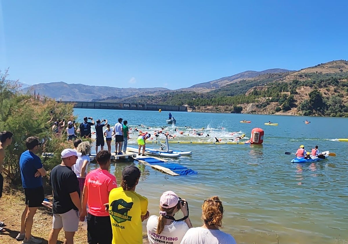 Una competición de natación es observada por varios piragüistas en el embalse