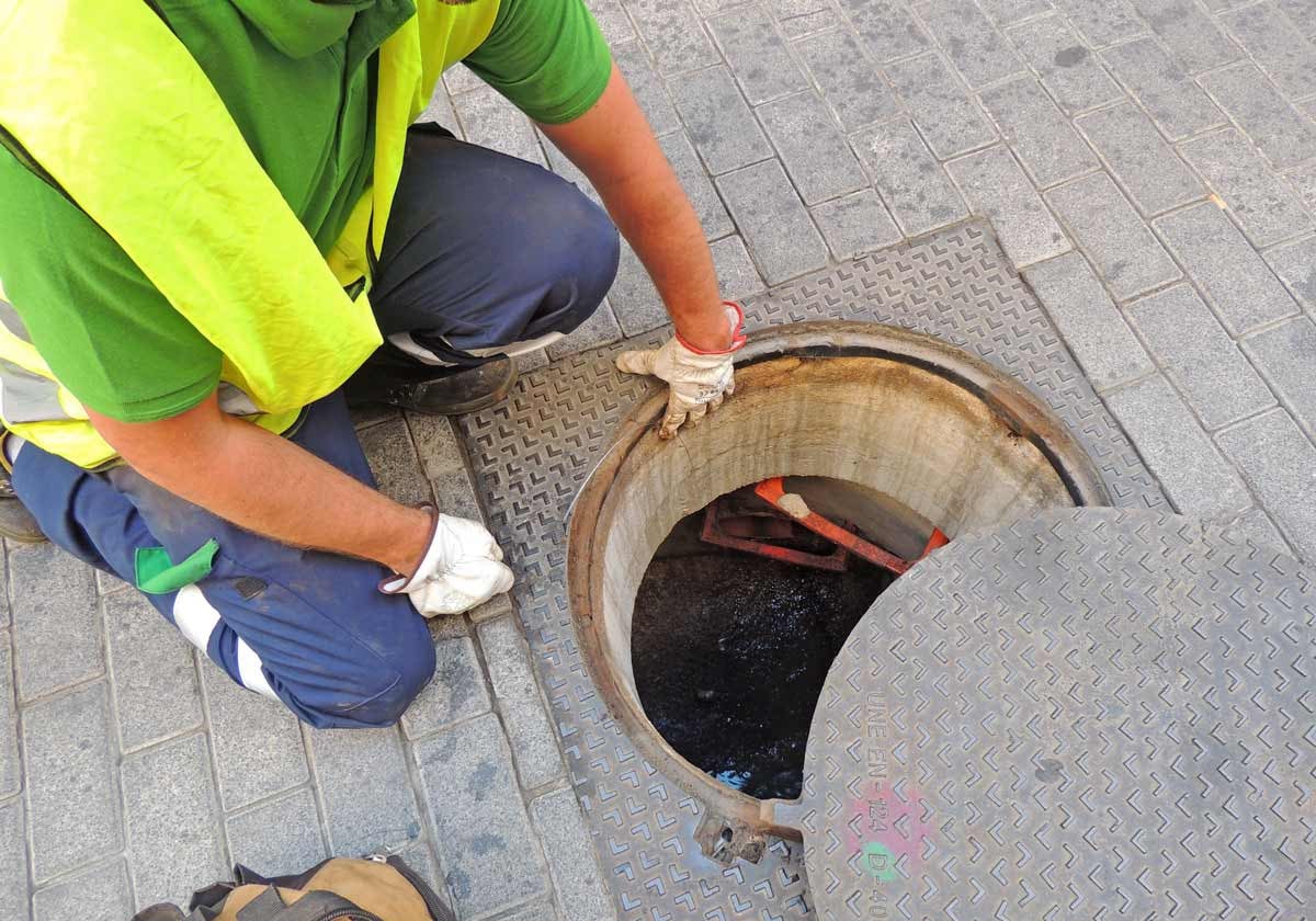 Un operario abre una alcantarilla en una calle de la capital