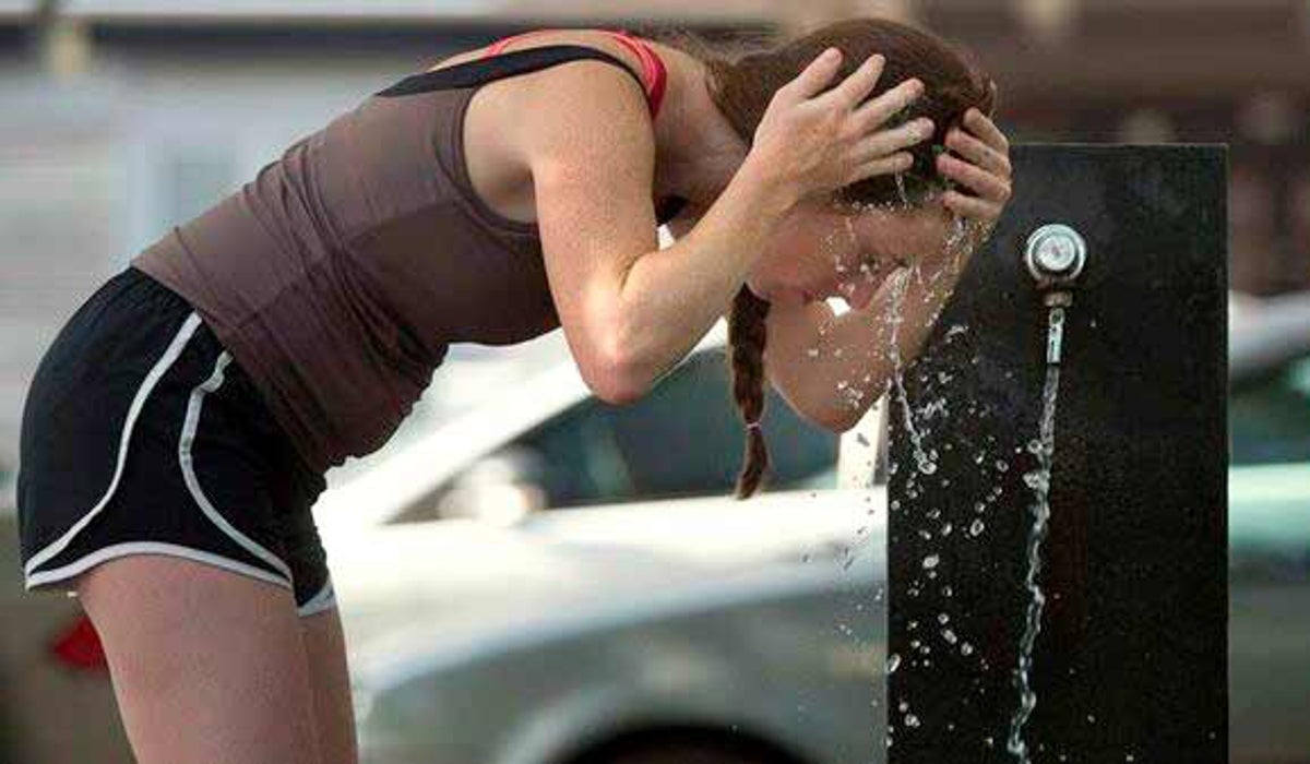 Una chica se refresca en una fuente pública