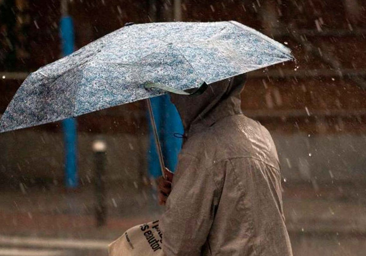 Un hombre camina por la calle resguardado bajo un paraguas