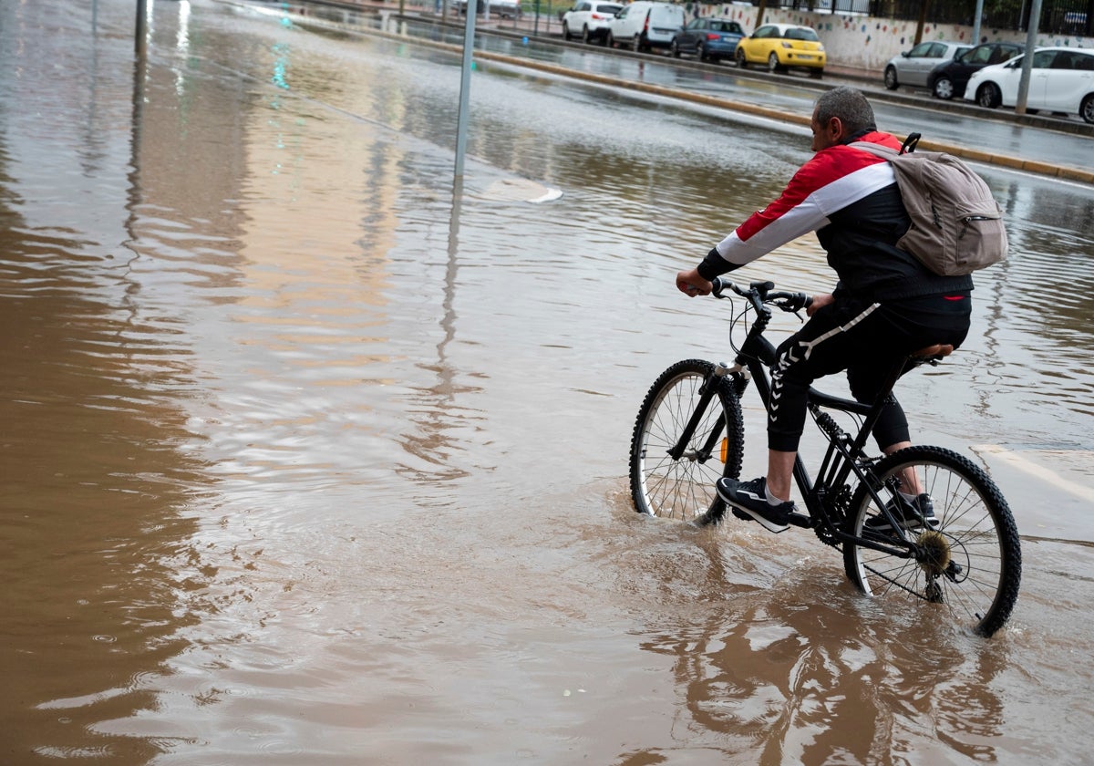 Un ciclista trata de cruzar una calle anegada por el agua
