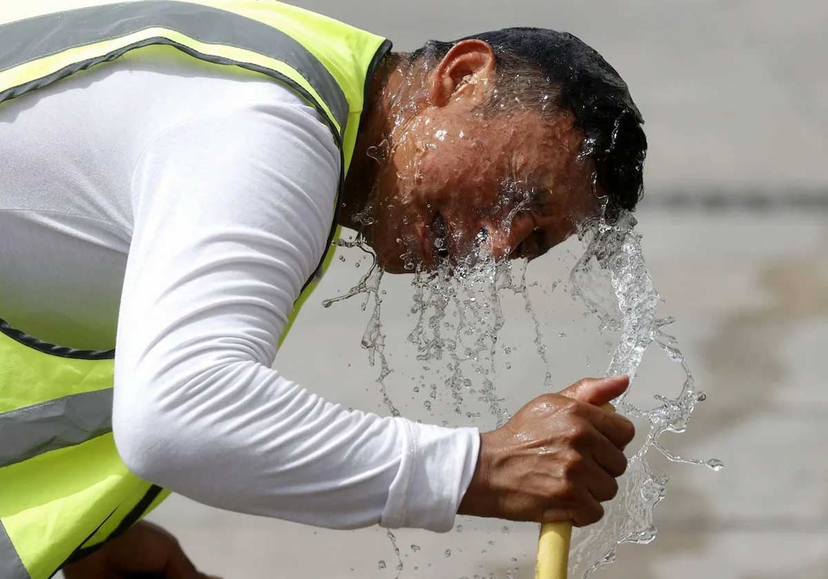 Un hombre se refresca con una manguera