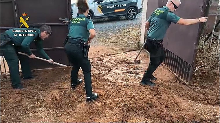 Tres agentes de la Guardia Civil quitando el lodo de la puerta de acceso a la finca en el término municipal de Gibraleón