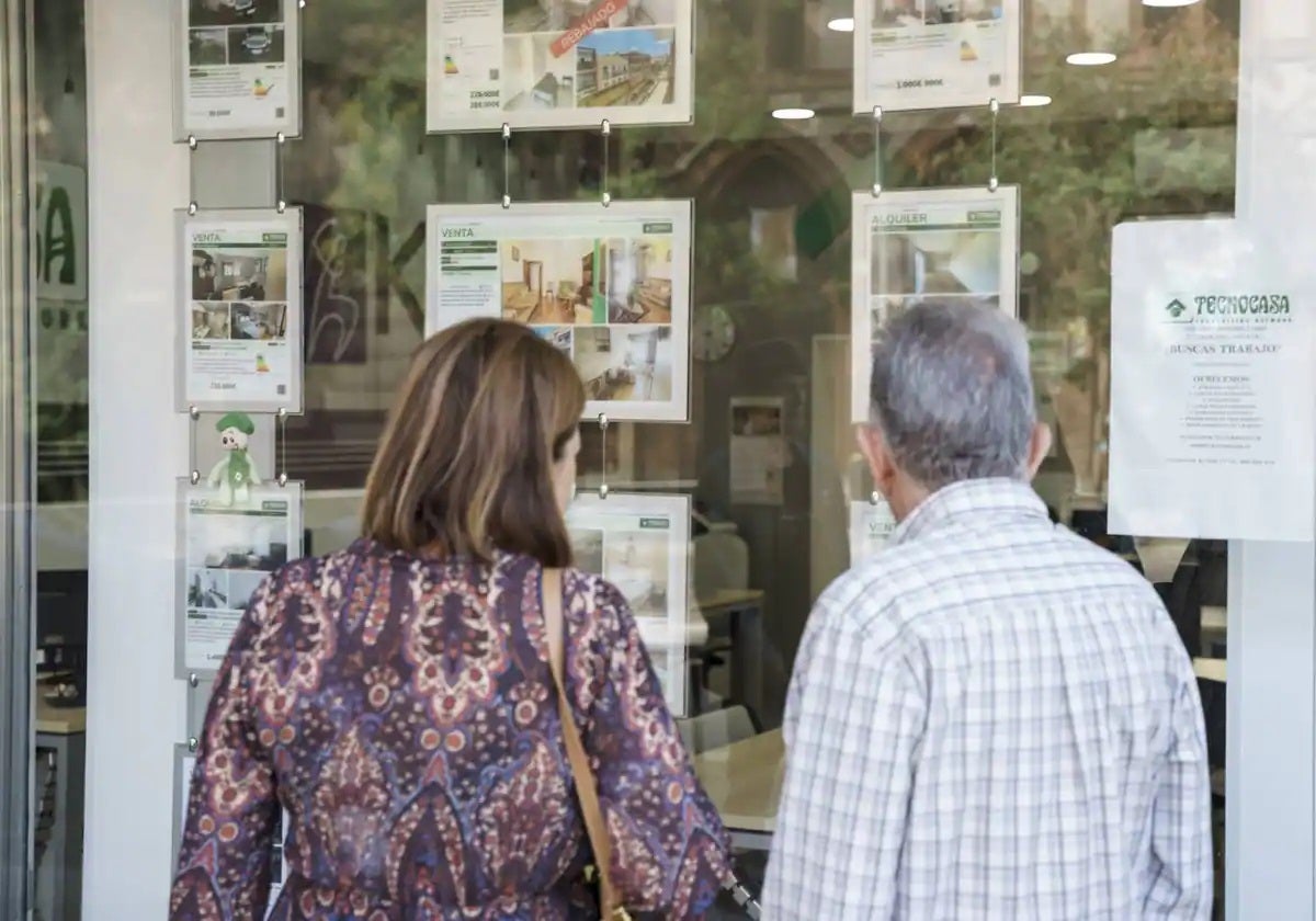 Personas mirando pisos de alquiler en el escaparate de una inmobiliaria de Cádiz