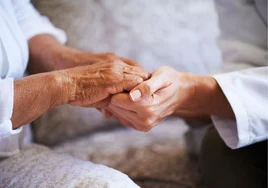 Las manos de una asistenta de ayuda a domicilio agarrando las manos de una persona mayor