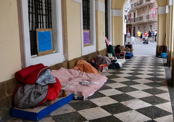 Personas sin hogar con sus enseres este viernes bajo los arcos de la fachada de la Casa Consistorial gaditana.
