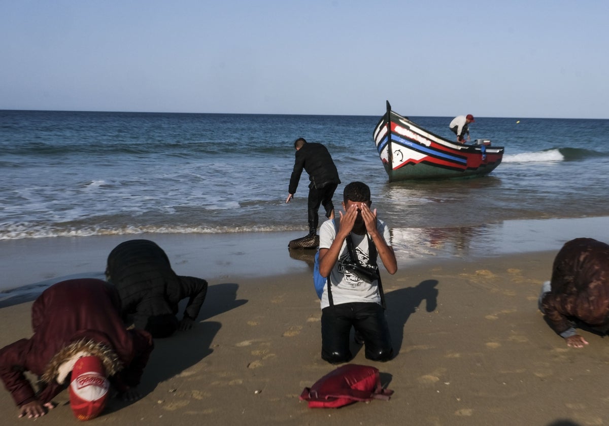 Unos migrantes rezan y besan el suelo al llegar a la playa de la Victoria de Cádiz en patera.