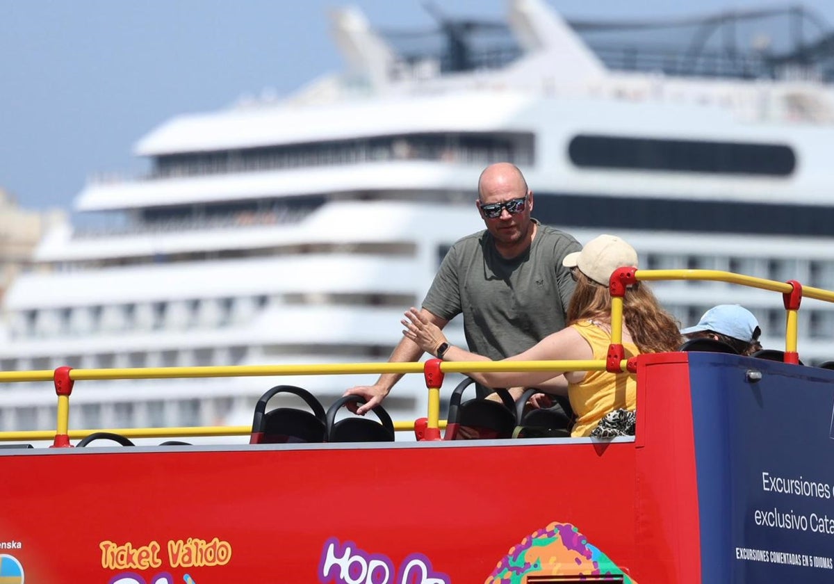 Una familia, subida en un autobús turístico con un crucero en el muelle de Cádiz de fondo