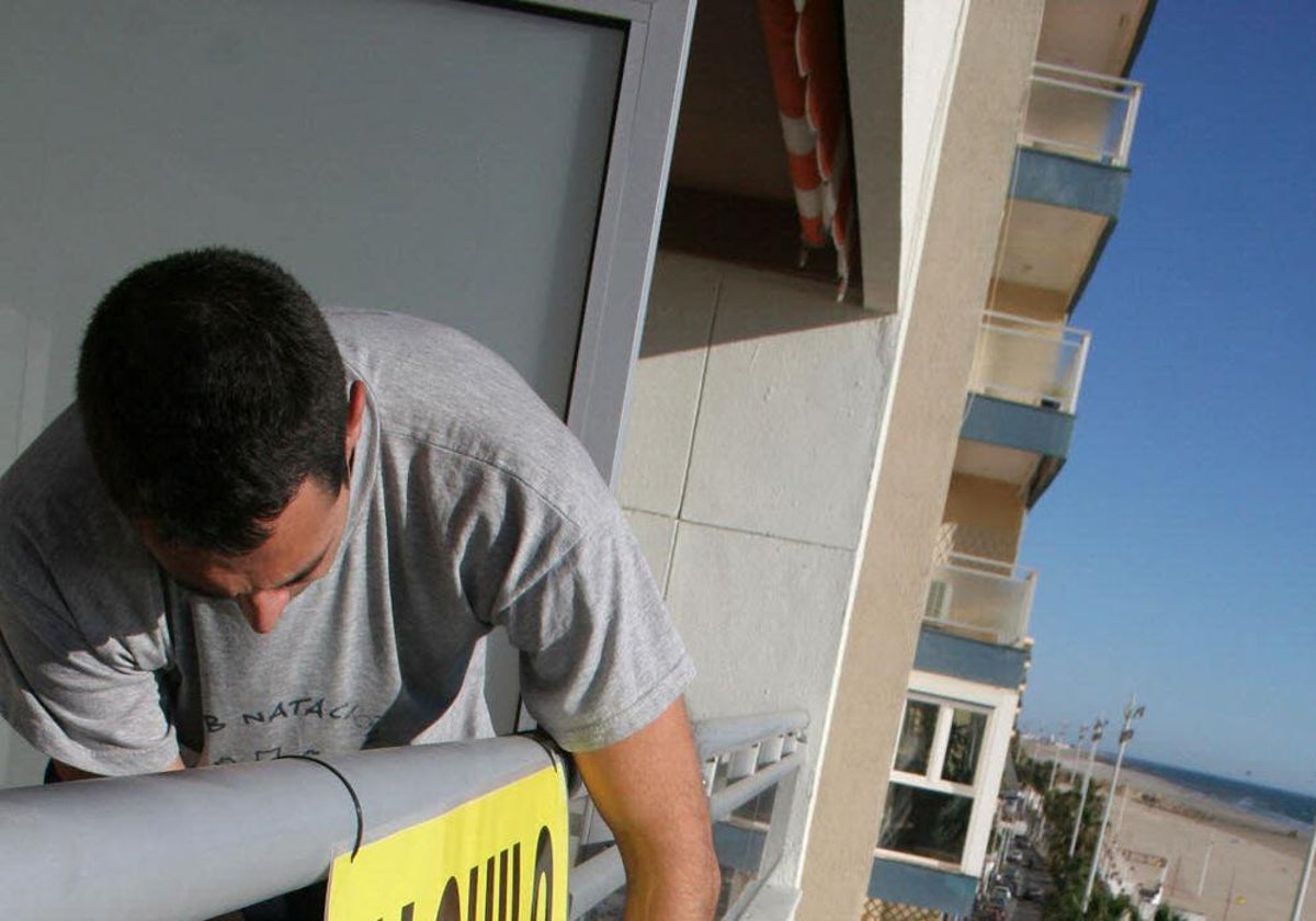 Un hombre coloca un cartel de 'Se Alquila' en una vivienda ubicada en el Paseo Marítimo de Cádiz.