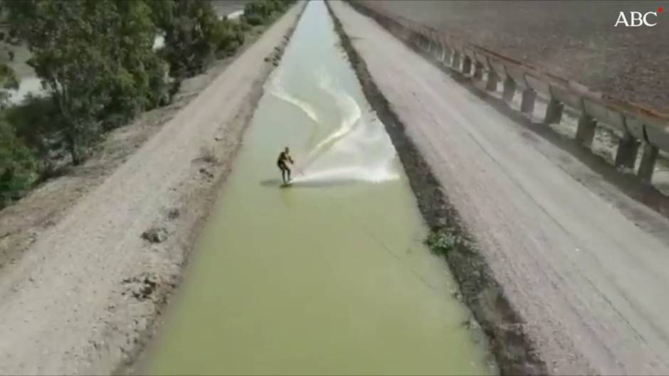 Unos surfistas recorren los canales de desagüe de las marismas del Guadalquivir a la altura de El Trobal