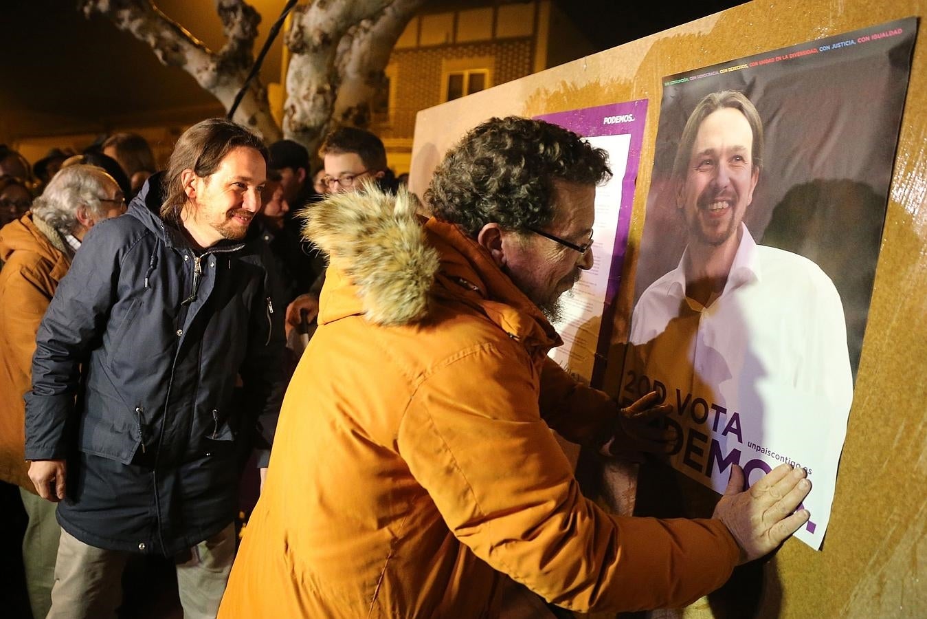 El padre de Pablo Iglesias pega un cartel con el rostro de su hijo durante el acto de inicio de campaña electoral de Podemos en un pequeño pueblo de Zamora. 